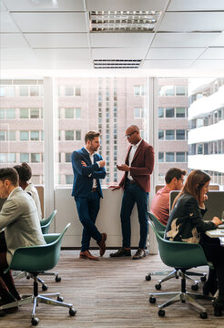 Business owners in formal suits chatting and browsing smartphone in busy office
