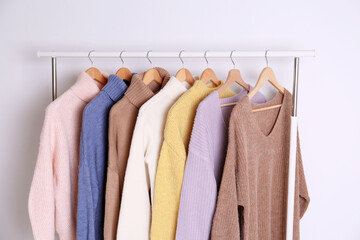Warm sweaters hanging on rack against white background