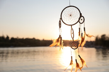 Beautiful handmade dream catcher near river on sunny day. Space for text