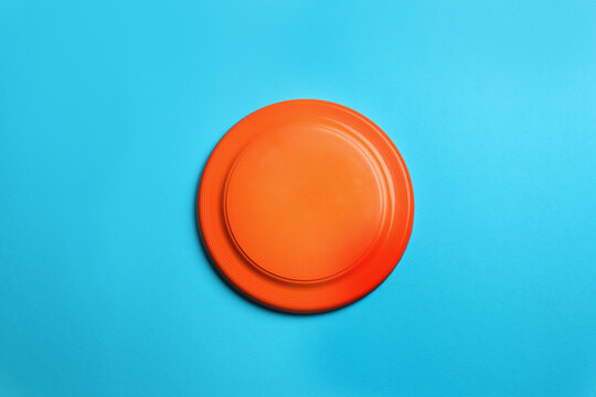 Orange plastic frisbee disk on light blue background, top view