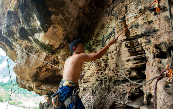 Confidence Asian Man Climber Preparing For Climbing Up The Rocky Mountain With Safety Rope And Harness At Tropical Island. Healthy Male Enjoy Active Lifestyle And Extreme Sport In Holiday Vacation.