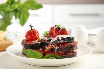 Baked eggplant with tomatoes, cheese and basil served on kitchen table, closeup