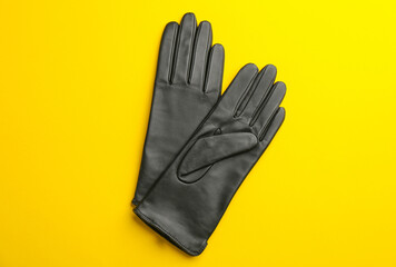 Pair of stylish leather gloves on yellow background, flat lay
