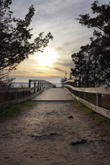 Wooden bridge with sandy path and the sun visible on the horizon during sunset