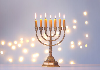 Golden menorah with burning candles against light grey background and blurred festive lights