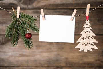 Fototapeta na wymiar Blank Christmas card and festive decor on rope against wooden background. Space for text