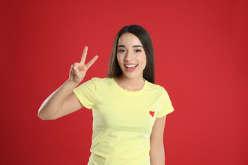 Woman in yellow t-shirt showing number two with her hand on red background