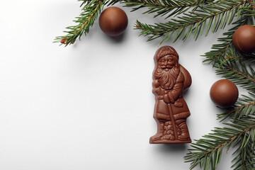Flat lay composition with chocolate Santa Claus, fir tree twigs and sweets on white background, space for text - Powered by Adobe