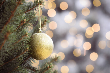 Shiny green ball hanging on Christmas tree against festive lights. Space for text