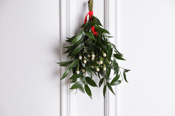 Mistletoe bunch with red ribbon hanging on light background. Traditional Christmas decoration
