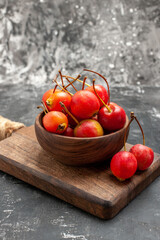 Vertical view of red cheries in a brown bowl and on small cutting board on gray background