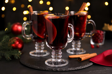 Aromatic mulled wine on black table against blurred festive lights