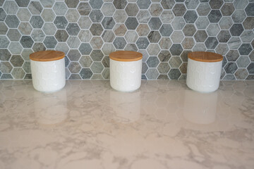 Modern kitchen detail of marble counter with hexagon tile backsplash and set of three white jars...