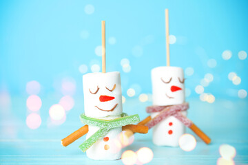 Funny snowmen made of marshmallows on light blue background, closeup. Bokeh effect