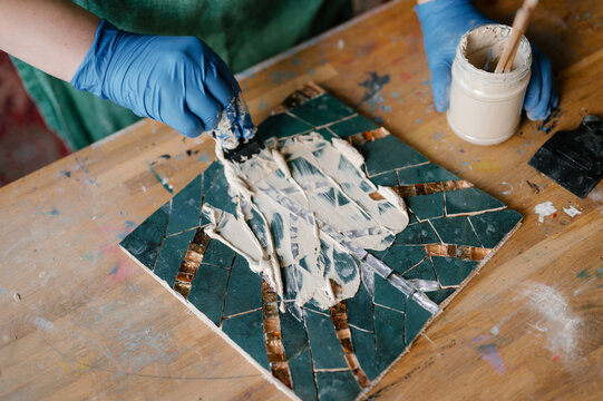 Crop artisan spreading cement on mosaic