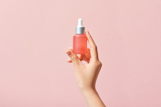 Woman hands holding facial essential oil on pink background.