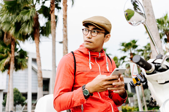 Stock photo of asian guy texting mobile phone in the city. He is sending a message.