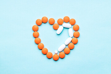 half heart symbol formed orange pills or tablets isolated on a blue background. above view. outer space. cardiac medicine concept