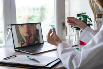 Young female dentist showing dental floss to patient through video call on laptop at home