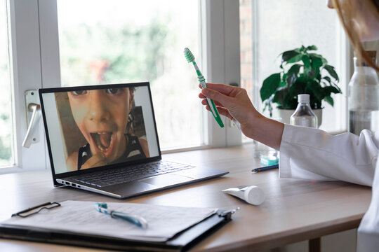 Female dentist showing toothbrush to patient through video call