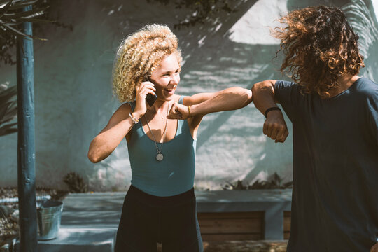 Smiling woman giving elbow bump to man while talking on mobile phone outdoors
