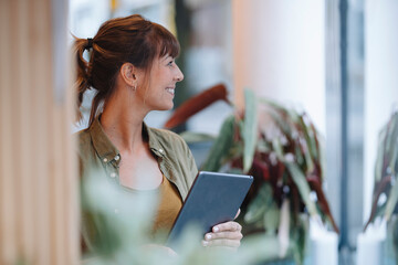 Female entrepreneur looking away while holding digital tablet standing in coffee shop