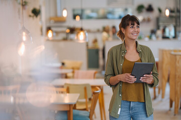 Smiling female entrepreneur looking away while holding digital tablet standing in cafe