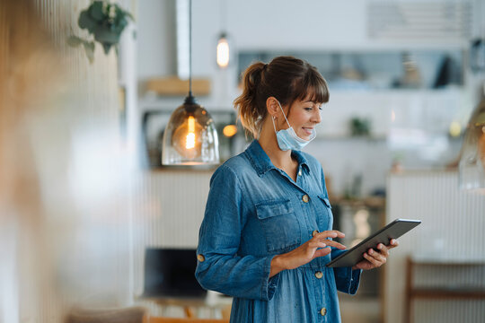 Female entrepreneur wearing protective face mask using digital tablet while standing in cafe