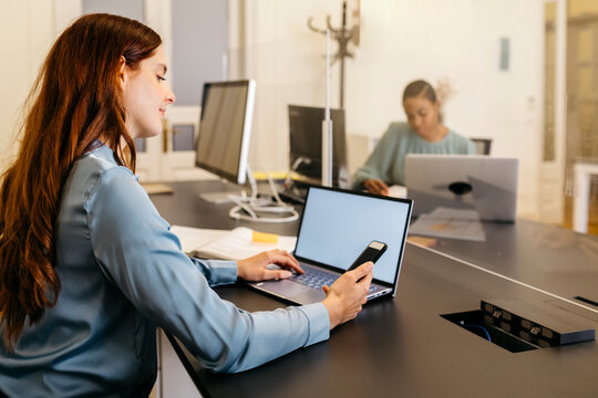 Businesswoman using smart phone and laptop while sitting at office desk