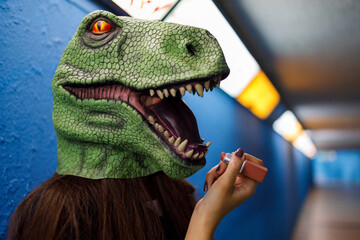 Woman applying lipstick while wearing dinosaur mask against blue wall