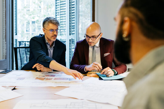 Businessmen discussing while looking at blueprint over table against window in office