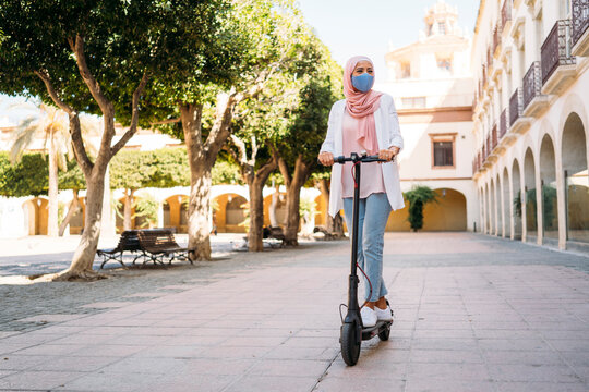 Young woman wearing face mask riding push scooter in city