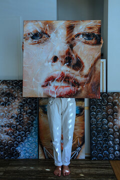 Female Artist Standing Behind Painting Against Wall In Art Studio