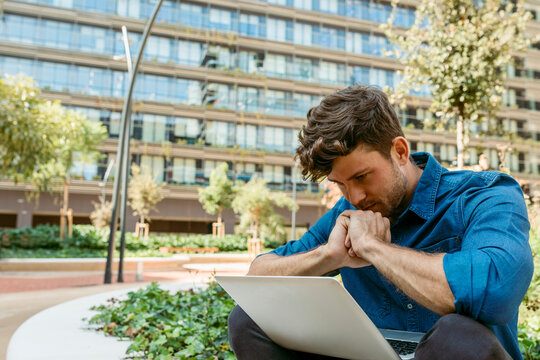 Businessman thinking while looking at laptop against office building