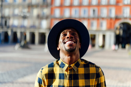 Smiling african man wearing hat looking up while standing in city