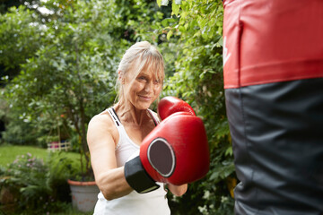 Senior woman punching punch bag while standing in back yard on sunny day