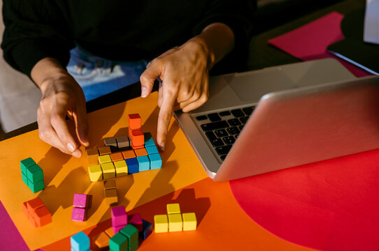 Hands of businesswoman playing with colorful toy blocks by laptop at table