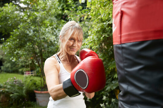 Senior woman punching punch bag while standing in back yard on sunny day
