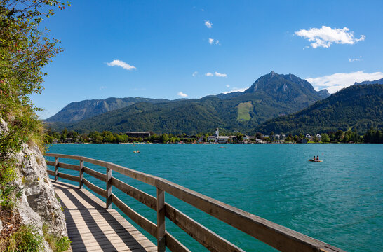 Austria, Salzburg, Strobl Am Wolfgangsee, Boardwalk stretching along shore of Lake Wolfgangsee in summer with forested mountains in background