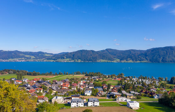 Drone view of town by lake and mountains against blue sky on sunny day, Attersee, Salzkammergut, Austria