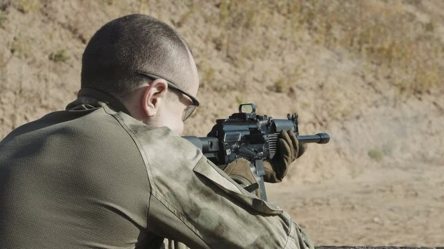 Rear view of a young man in camouflage clothes aiming and shooting outdoors alone.