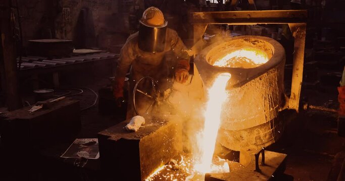 Close-up front view of a factory worker pouring molten metal into casts at a steel casting foundry