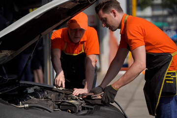 Two men are car mechanic Use a wrench and a cord to check the car battery.