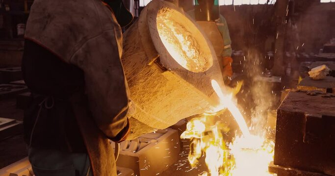 Close-up side view of factory workers pouring molten metal into casts at a steel casting foundry