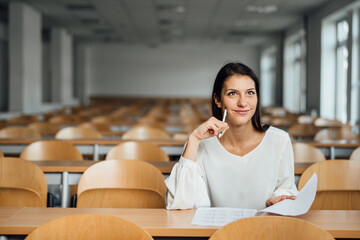 Knowledgable female student taking an easy exam in an empty amphitheater. An optimistic student taking an in-class test. Happy woman having stress free education evaluation.Essay exam inspiration.