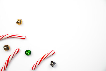 Beautiful holiday background of candy cane peppermint sticks, and green, gold and silver jingle bells with white open copy space to the right.