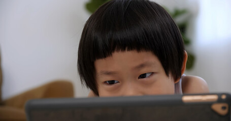 Cute little boy using tablet computer at home.