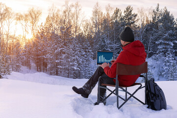 Adult blogger or freelancer working on a laptop at winter nature. Man working outdoors. Concept remote work.