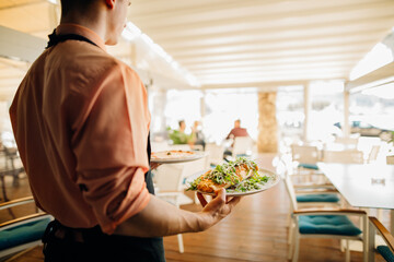 Waiter serving lunch to the distant customer.Empty restaurant due to safety restrictions. Small business working at lower capacity.No customers in the pizzeria.Waiter serving pizza.Eating out
