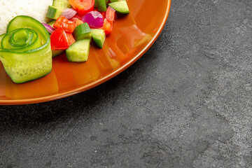 Half shot of homemade rice dish and salad with tomato and cucumber on dark table